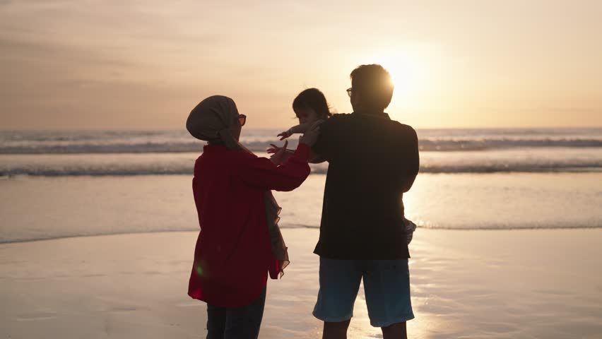 Happy Modern Muslim Southeast Asian Indonesian Family Enjoying Sunset Together on The Beach. Silhouette of Father Mother and Child in Slow Motion. Royalty-Free Stock Footage #1099584703