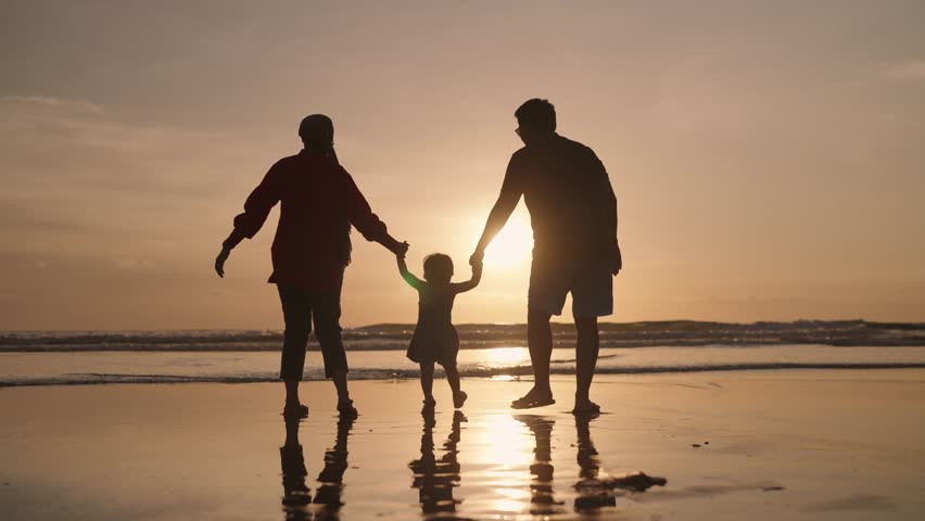 Happy Modern Muslim Southeast Asian Indonesian Family Enjoying Sunset Together on The Beach. Silhouette of Father Mother and Child in Slow Motion. Royalty-Free Stock Footage #1099584709