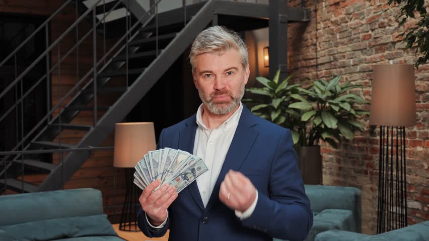 A middle-aged businessman holds a large wad of money in his hands and talks about the possibility of earning money on crypto exchanges, stock market and online casino. Easy winnings in the lottery. | Shutterstock HD Video #1099585921