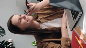 Vertical video of happy young woman work online on computer in home office, record audio voice message on smartphone. Cute smiling female employee buys with laptop talk on loudspeaker on cellphone - Powered by Shutterstock - Get 15% off with code: PIKWIZARD15