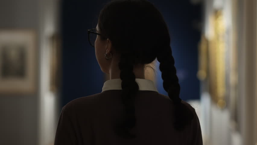 History and culture. Back view of woman walking in museum and contemplating masterpiece arts. Visiting excursion in art exhibition. Concept of educational and cultural tourism.