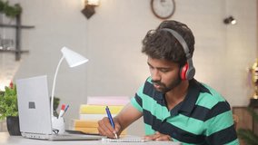 College student interacting during online class while listening on laptop by writing notes - concept of distance education, e-learning and technology or internet