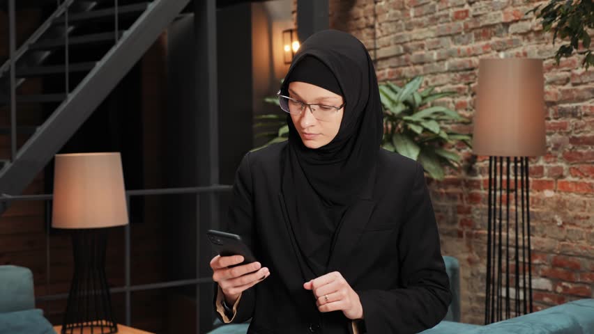 Surprised Muslim Islamic woman winner hold smartphone read good news feels euphoric amazed by mobile online bet bid game win winner, overjoyed by victory success. Financial stock sports betting. | Shutterstock HD Video #1099588913
