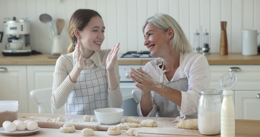 Overjoyed middle-aged mother clap hands, having fun with happy teenage 13s daughter, making together sweets biscuits or buns. Family in aprons cooking at home, spend weekend prepare homemade pastries | Shutterstock HD Video #1099588933