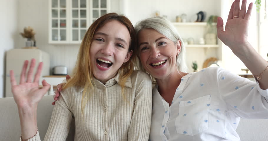 Mature woman with teen daughter making video call sit on sofa at home, wave hands greeting family living abroad feel happy enjoy distancing communication using modern technology, virtual meeting event | Shutterstock HD Video #1099588947