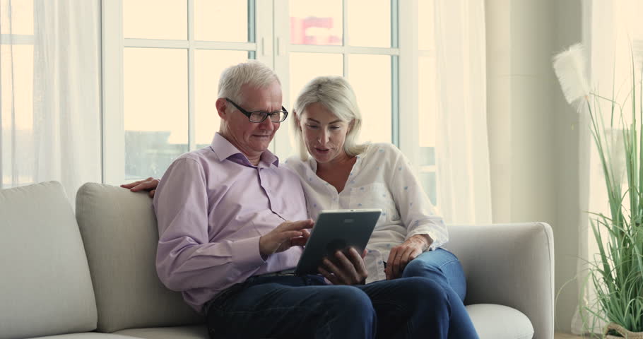 Middle-aged woman and older dad use digital tablet at home, buy services, order goods via retail services e-commerce app spend time together enjoy easy e-shop. Generations use modern tech, lifestyle | Shutterstock HD Video #1099589023