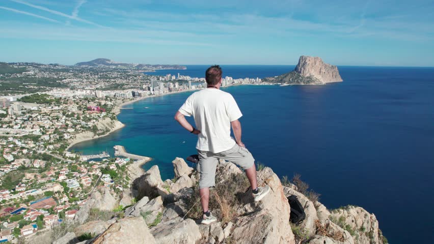 A man stands on the edge of a cliff overlooking the ocean. Tourist on top of the mountain with seascape. Success victory achievement concept. | Shutterstock HD Video #1099589615
