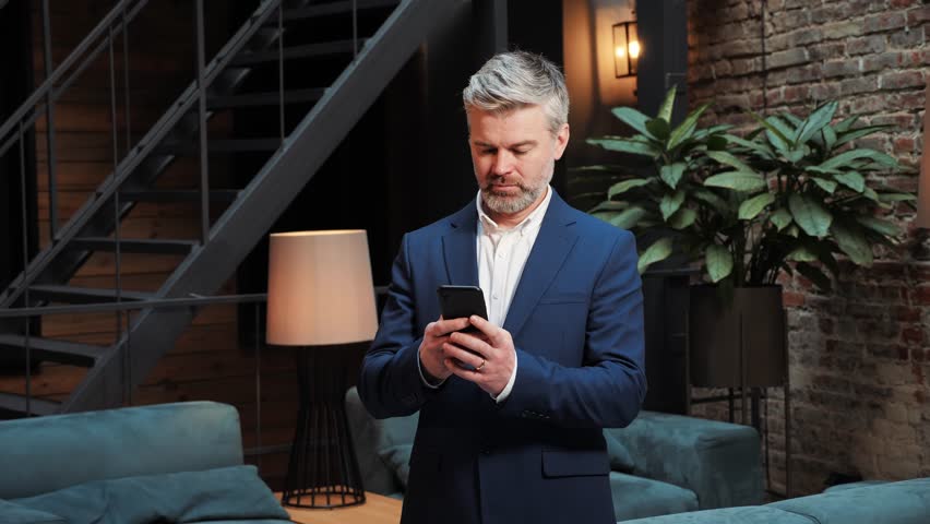Happy confident focused business man entrepreneur investor holding smartphone using mobile app looking at cell phone working with online digital financial data management technology working in office. | Shutterstock HD Video #1099589927