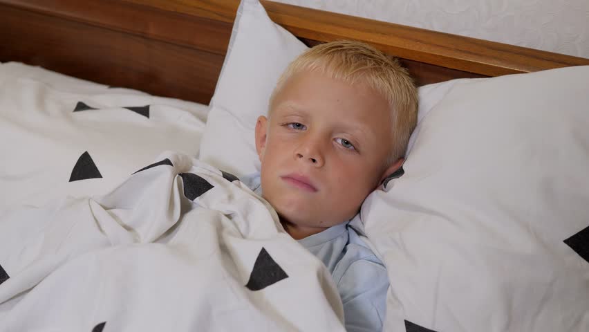 A little boy with a fever is sleeping in a bed at home, he is covered with a blanket. | Shutterstock HD Video #1099590435