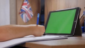 A school-age boy remotely studies online at home, he writes in a notebook sitting in front of a tablet with a green screen. Distance learning of children in quarantine according to covid-19. - Powered by Shutterstock - Get 15% off with code: PIKWIZARD15