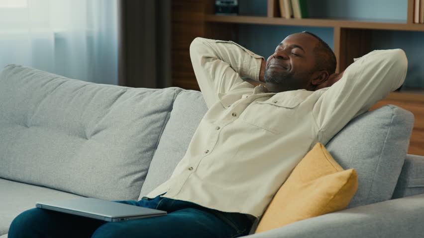 Mature african american man relaxed businessman freelancer resting on couch with hands behind head distracted from work on laptop taking break napping dozing dreaming reducing fatigue feeling peaceful | Shutterstock HD Video #1099590775