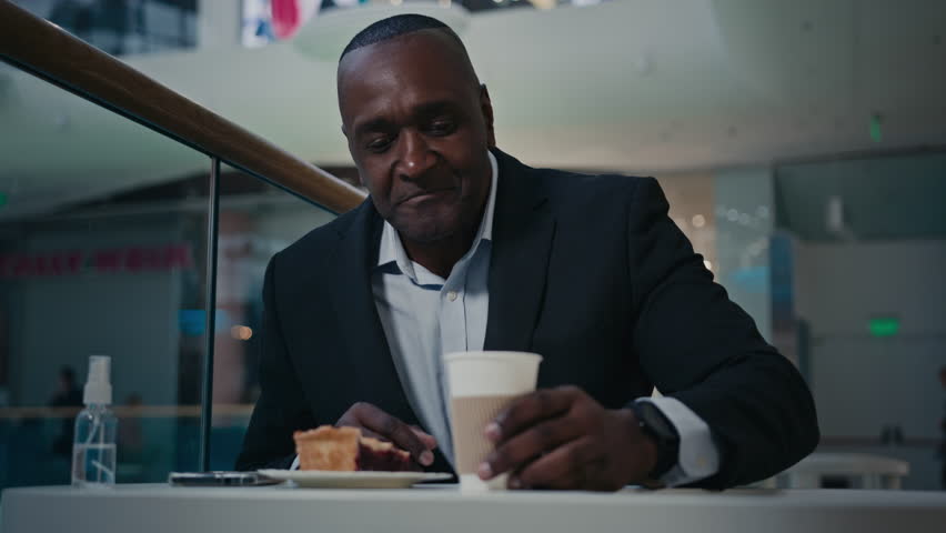 African middle-aged businessman in cafe browsing chatting with mobile phone waitress brink pie cake and drink man taste coffee enjoy drinking showing thumb up satisfied with cappuccino in cafeteria | Shutterstock HD Video #1099590783