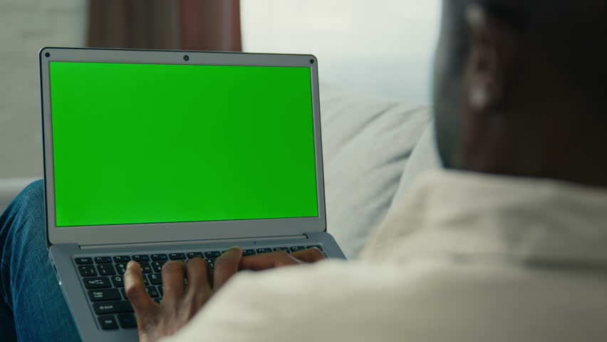 Over shoulder shot african american man businessman programmer freelancer typing on laptop work remote at home on couch looking at green mock-up screen chroma key browsing website make order online | Shutterstock HD Video #1099590801