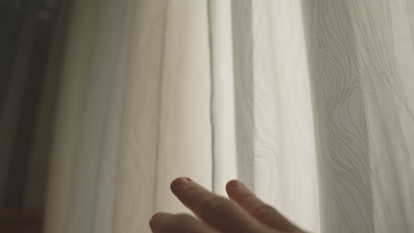 Hand reaching slowly towards a window curtain and opens it to reveal sunlight. Symbol of hope, positivity green energy or bright future. Pulling window shade to look outside in bright morning sun Royalty-Free Stock Footage #1099591773