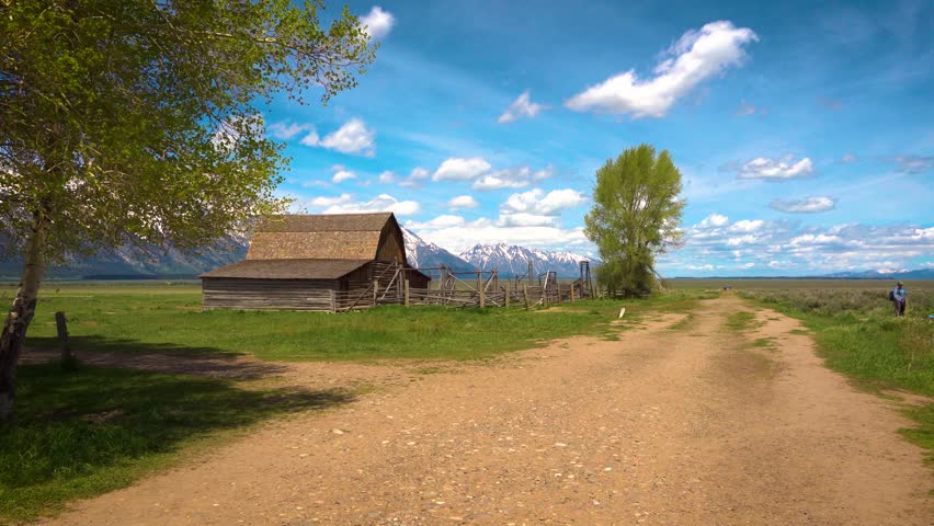 Approaching Historic John Moulton Barn at Mormon Row in Grand Teton National Park on a sunny summer day, with snowcapped Teton Mountain Range in the background. 4K UHD video.