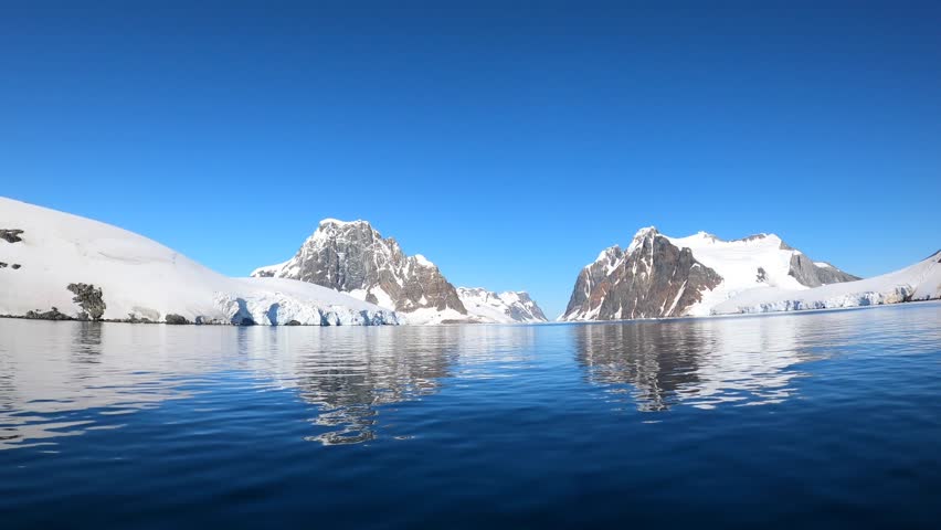 Antarctica landscape water surface and snow-capped mountains time lapse. Amazing calmness characteristic of Antarctica is given by clear blue sky. | Shutterstock HD Video #1099592963