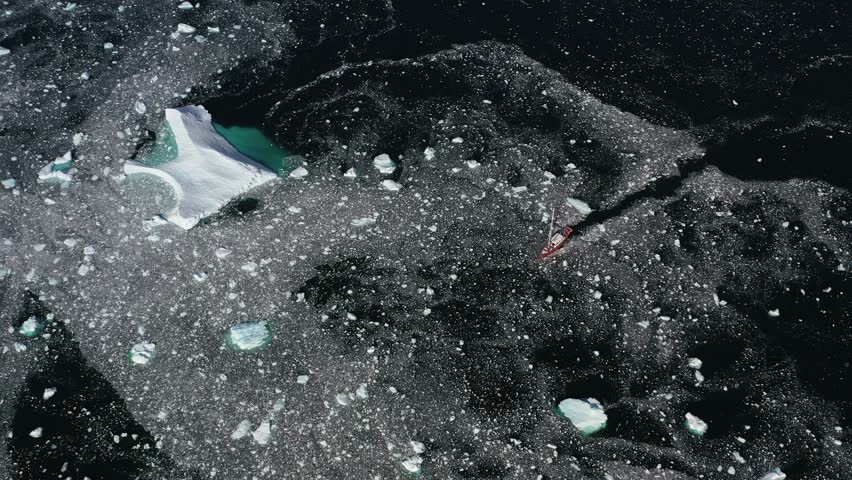 Ship floats in Antarctica, drone footage. Top view of ship floating among small pieces of ice in Antarctica. Antarctica consists of mainland and adjacent islands that are washed by oceans.