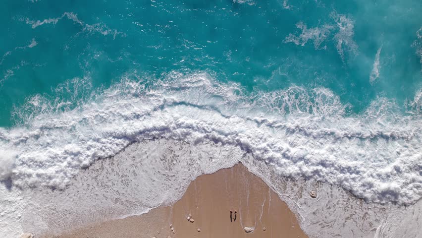 Amazing sea Aerial top view ocean blue waves break on a sandy beach waves crashing against a beach.The couple is standing on the seashore. Sea waves and beautiful romantic sand beach  | Shutterstock HD Video #1099593545