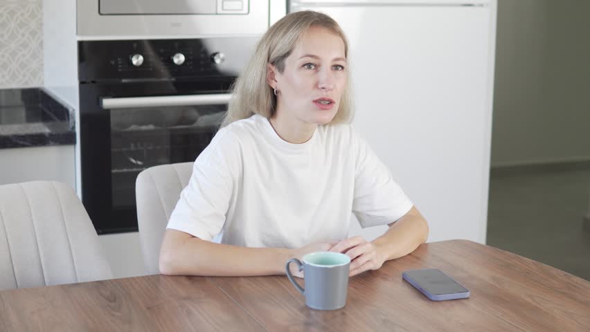 An agitated Woman sits at a table in the morning. | Shutterstock HD Video #1099593843