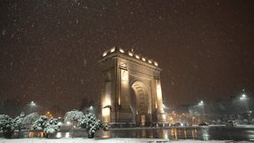 Winter night in Bucharest. 4K wide angle video during a beautiful snowfall in front of Arch of Triumph landmark from Bucharest, Romania, 2023.