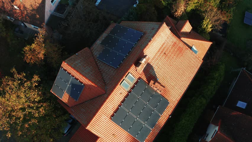 A cinematic drone shot of country houses with solar panels installed on rooftops in a modern city district. Flying over the solar panels on the roof of an apartment building.  Royalty-Free Stock Footage #1099597231