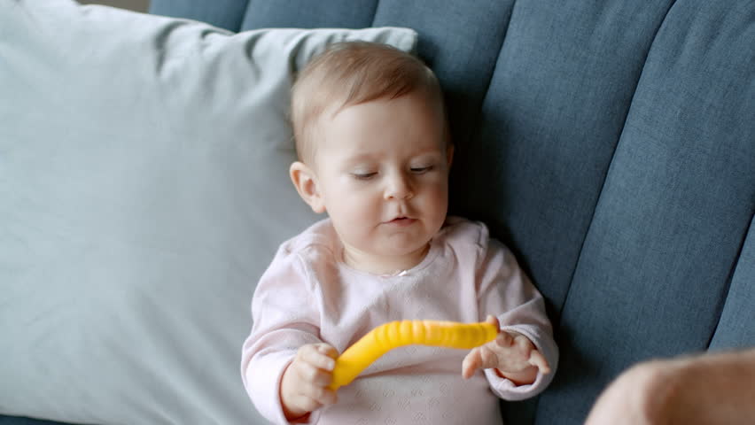 Health check. Close up portrait of adorable little baby girl playing with toy on sofa, dad hand measuring body temperature with contactless thermometer at home, slow motion, empty space | Shutterstock HD Video #1099598537
