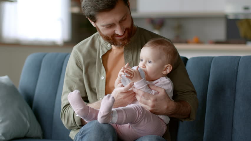 Baby care. Loving young father holding his little daughter on hands, adorable thirsty girl drinking water from bottle, resting together at home, tracking shot, slow motion, free space | Shutterstock HD Video #1099598543