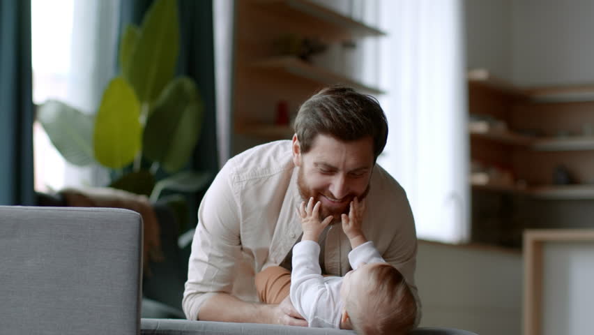Fatherhood and babysitting. Young happy dad playing with his newborn baby daughter, blowing at her, carefree girl laughing, slow motion, empty space | Shutterstock HD Video #1099598553