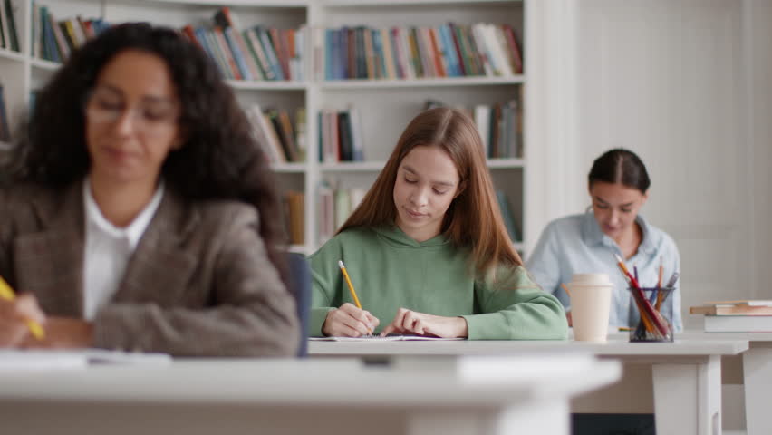 Incomprehensible topic. Tracking shot of group of female students studying at classroom, one lady raising hand and asking question, slow motion, selective focus, free space