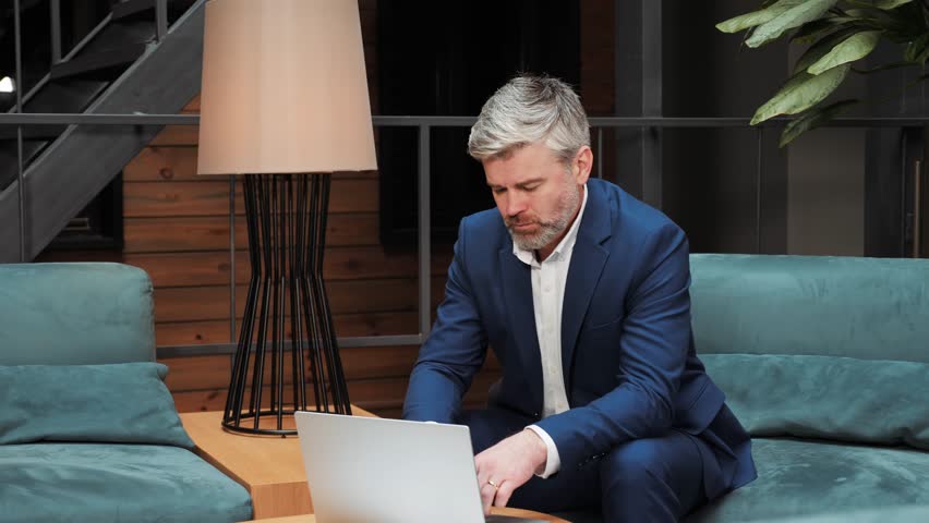 Thoughtful businessman sitting at conference hall with laptop computer. Pensive professional banker thinking about task solution. Focused business man finding inspiration solving a problem indoor. | Shutterstock HD Video #1099598653