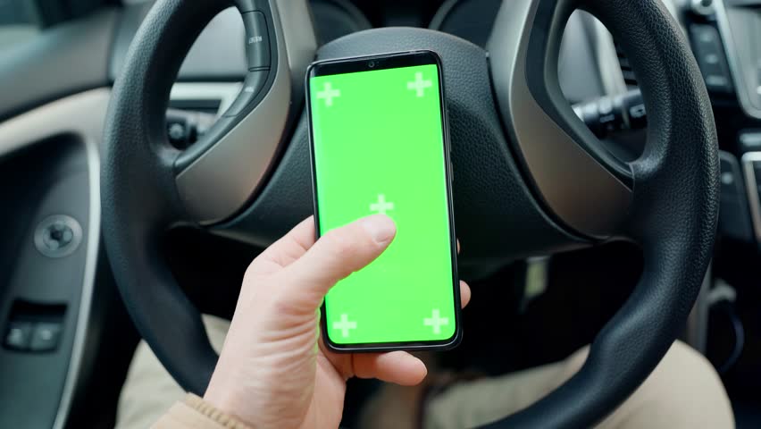POV man in car at driver place, holds a phone with green screen with marks in hand. driver holds phone against steering wheel, swiping by finger in different directions. navigation, shopping concept | Shutterstock HD Video #1099599015