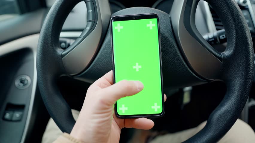 POV man in car at driver place, holds a phone with green screen with marks in hand. driver holds phone against steering wheel, swiping by finger in different directions. navigation, shopping concept | Shutterstock HD Video #1099599025