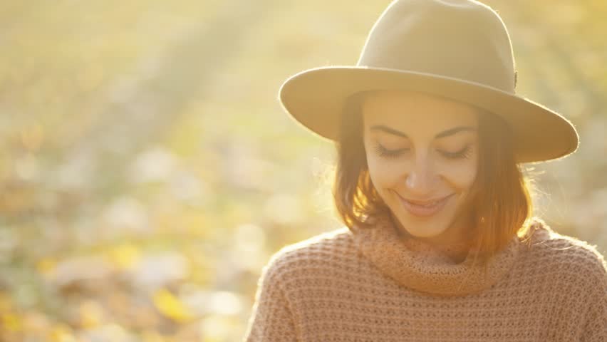 Close up autumn portrait of beautiful smiling woman wearing in wrown dress, sweater and hat. girl holds yellow leaves and playfuly looking at camera | Shutterstock HD Video #1099599055