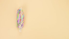 Hands opened small plastic bag with bunch of colorful rubber bands and por them out on yellow background. Bright office rubber bands. Multicolored elastic rubber bands close up.