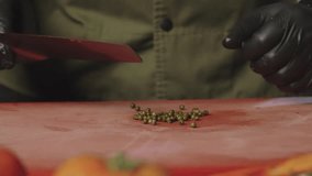 Slow motion video of the chef slicing black pickled pepper. Preparation of ingredients and spices for steak.
