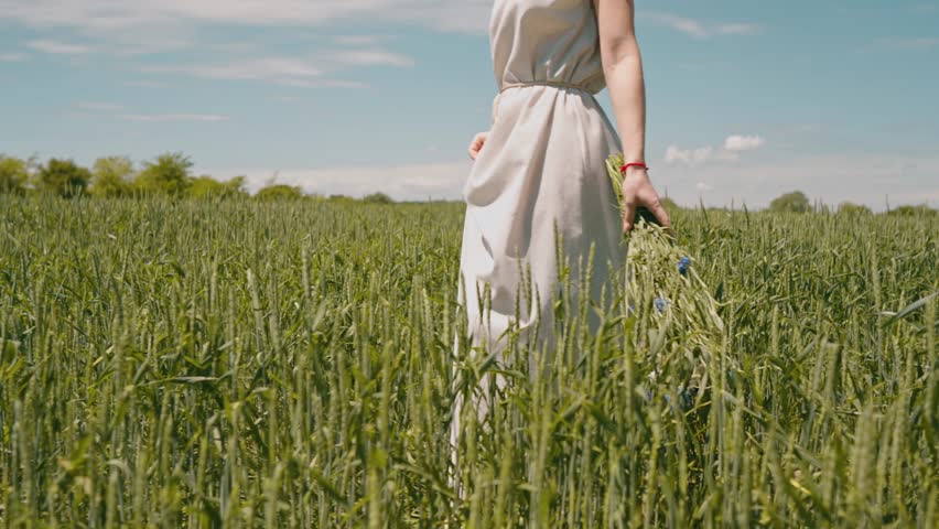 beautiful woman in a simple linen dress in a field with a bouquet of wildflowers in her hands, the concept of summer walks, folklore simple style