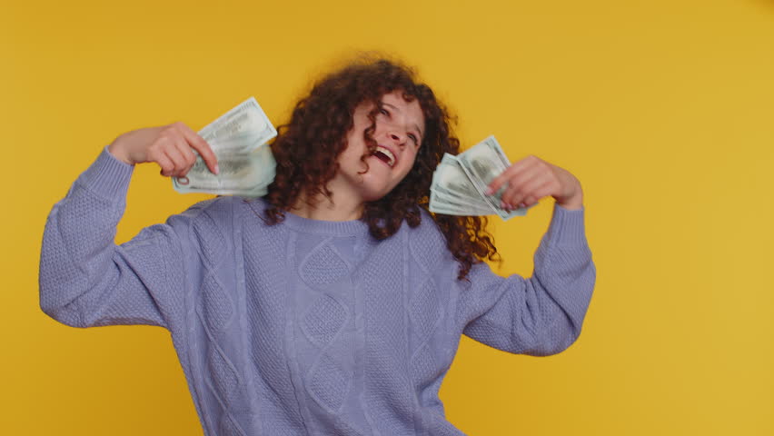 Rich pleased boss millennial woman waving money dollar cash banknotes bills like a fan, success business career, lottery winner big income wealth. Young curly haired girl isolated on yellow background | Shutterstock HD Video #1099602933