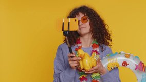 Happy young traveler blogger woman in sunglasses with swimming ring, luggage taking selfie on smartphone with subscribers record make video call online. Curly haired tourist girl on yellow background
