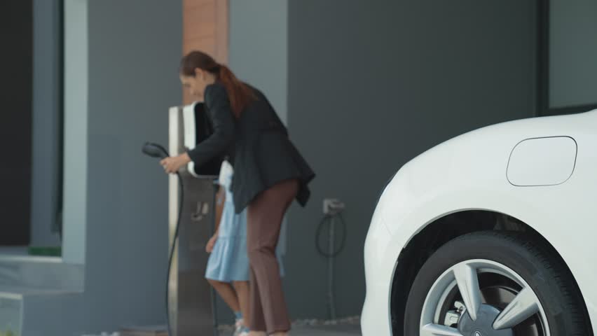 Progressive lifestyle of mother and daughter who have just returned from school in an electric vehicle that is being charged at home. Electric vehicle powered by sustainable clean energy. | Shutterstock HD Video #1099603507