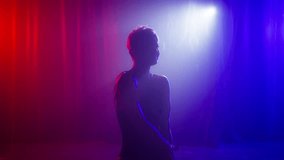 Perfect female body with neon beams glowing on background with falling rain droplets. Fashion Art Video slow. Dark silhouette of elegant girl dancing slowly in red blue neon lights on foggy background