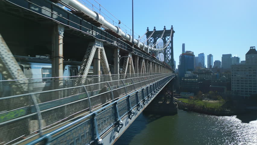 Forwards tight flight along subway train passing on Manhattan Bridge over East river. Large steel suspension bridge. New York City, USA Royalty-Free Stock Footage #1099605893