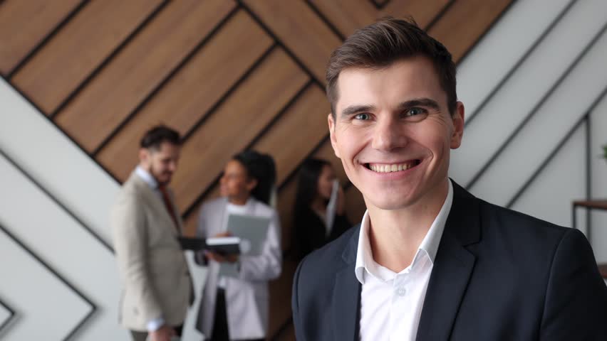 Portrait of a charismatic young businessman in a formal suit in an office setting in the background company employees condemning business issues | Shutterstock HD Video #1099606471