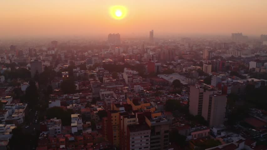 Awesome dynamic wide establishing shot of Mexico City at sunset. In frame yellow orb from the sun shining through the smog. Royalty-Free Stock Footage #1099609891