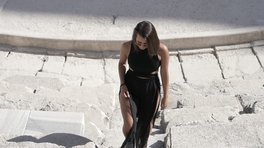 Young Woman in Black Dress Walking on Steps in Ancient Roman Theatre Auditorium, Close Up