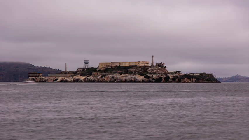 Famous landmark Alcatraz Island in the San Francisco Bay seen from San Francisco. Boats passing by, some rays of sunlight hitting the island.