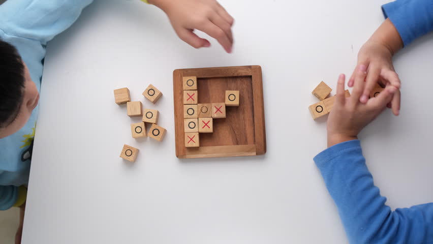 Little siblings playing wooden board game tic-tac-toe on table in living room. Family spending time together on weekend. | Shutterstock HD Video #1099610549