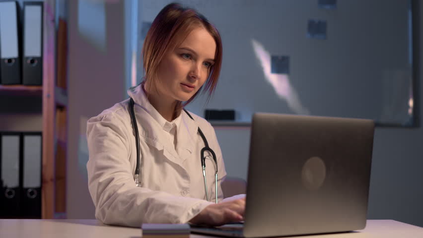 Female doctor working with laptop computer and typing information from paperwork. Hospital night background. | Shutterstock HD Video #1099612509