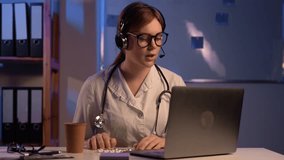 Young doctor or vet sitting with headset or headphones at her desk in front of a laptop computer make video call with a patient.