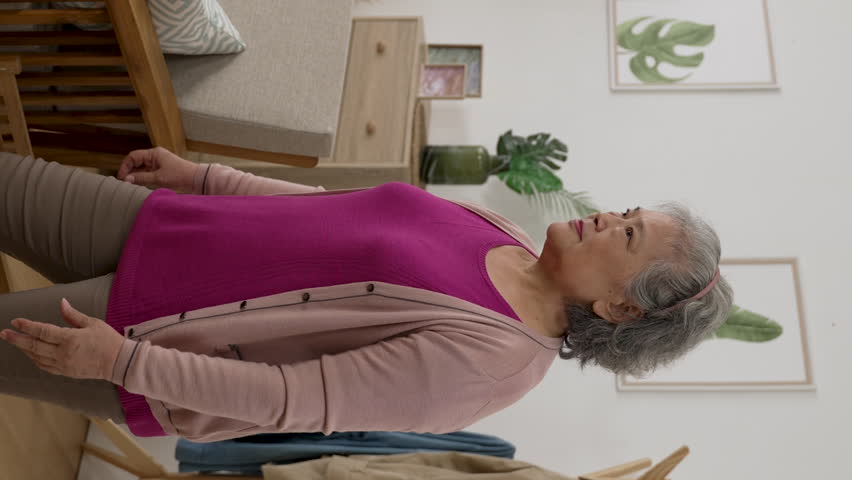 Vertical Screen: asian senior lady is feeling pain for she sprained her lower back while she is walking into the living room at home and supporting herself with sofa armrest | Shutterstock HD Video #1099616485