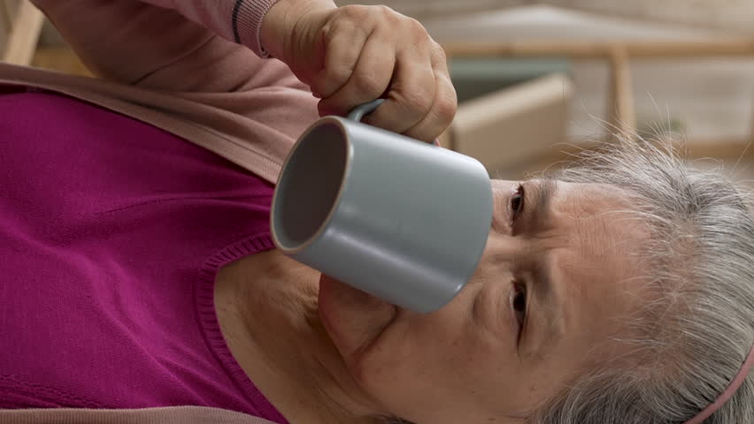 Vertical Screen: shoulder shot of a sick asian old lady having flu is soothing a cough by drinking water in the living room at home. retirement and healthcare concept | Shutterstock HD Video #1099616499